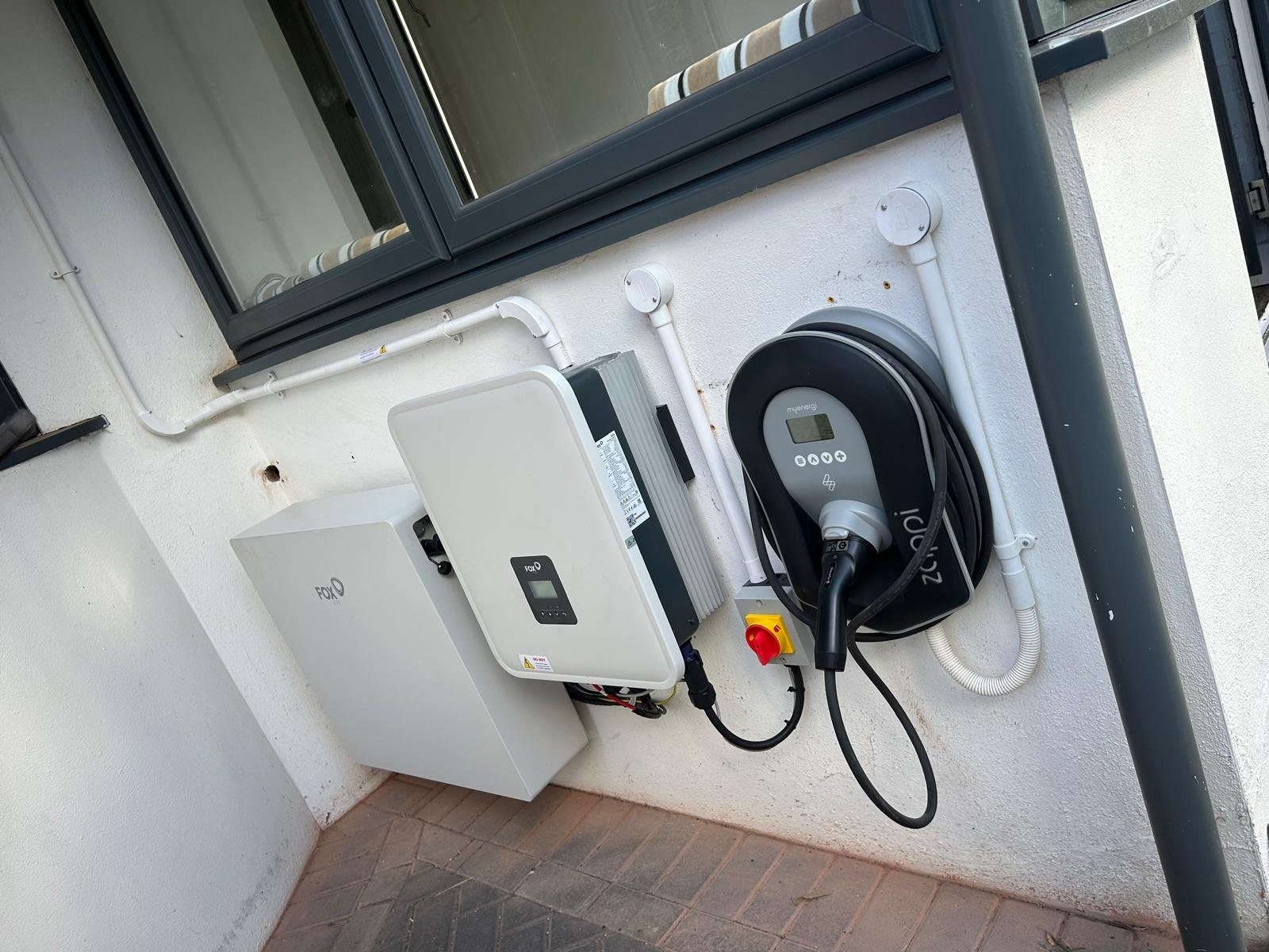 Fox ESS inverter and battery wired alongside a Zappi EV charger with isolator on a rendered wall in Winchester