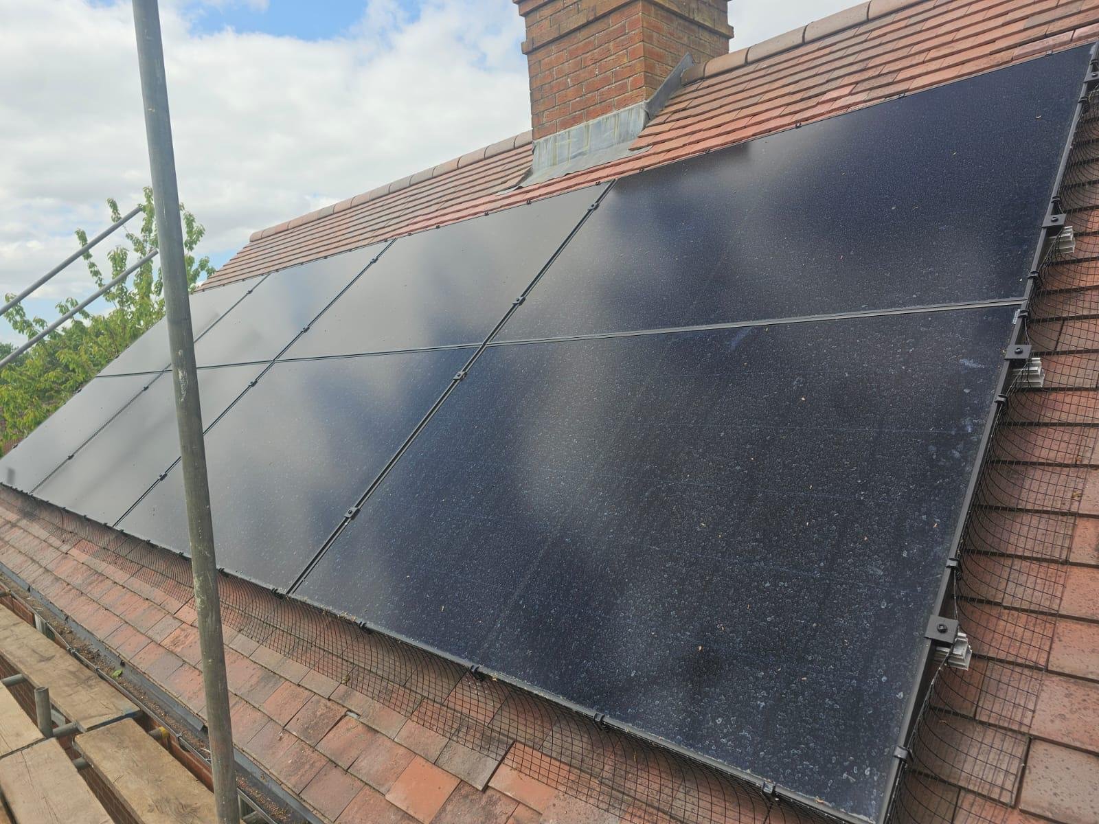Black solar panels fitted around a chimney on a red tiled roof