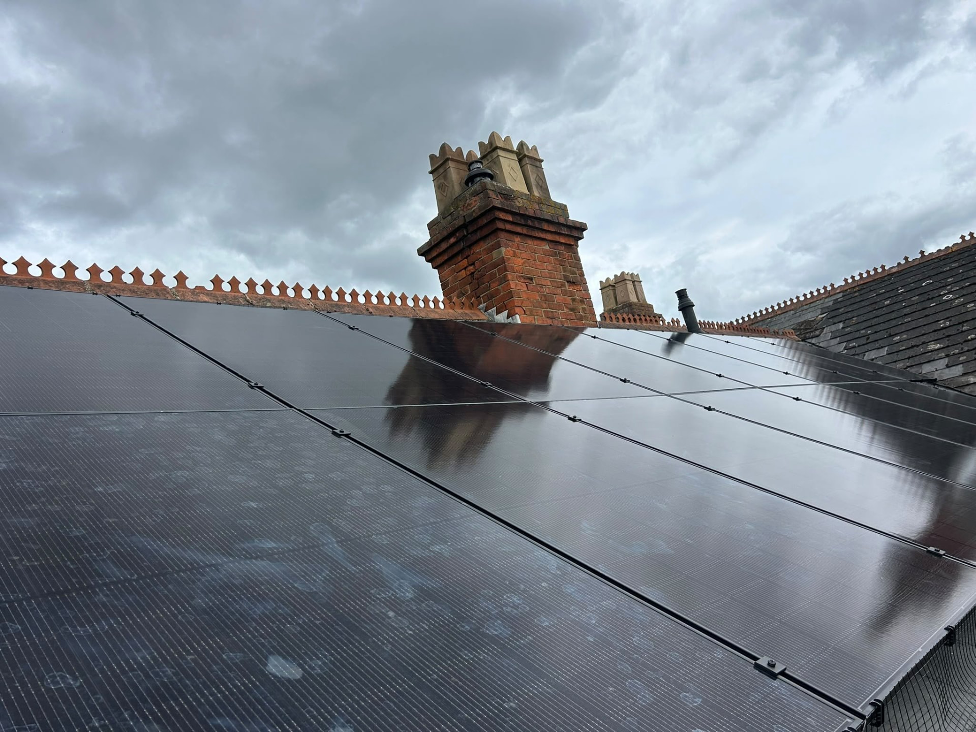 Completed solar PV array on a slate roof beside ornate brick chimneys