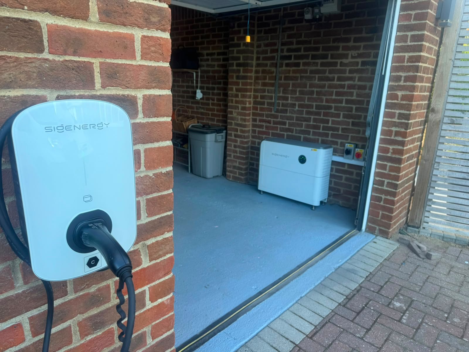 Sigenergy EV charger installed on a brick wall beside home battery storage