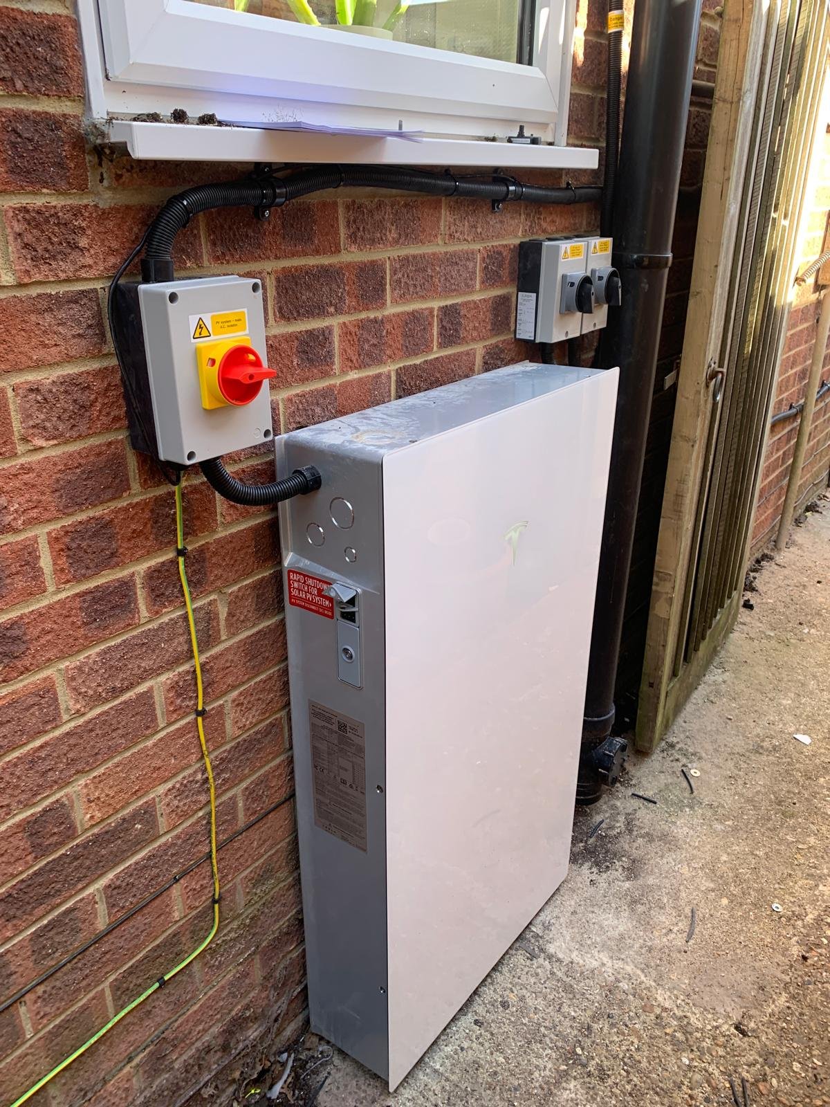 Tesla Powerwall home battery installed on an exterior brick wall in Winchester